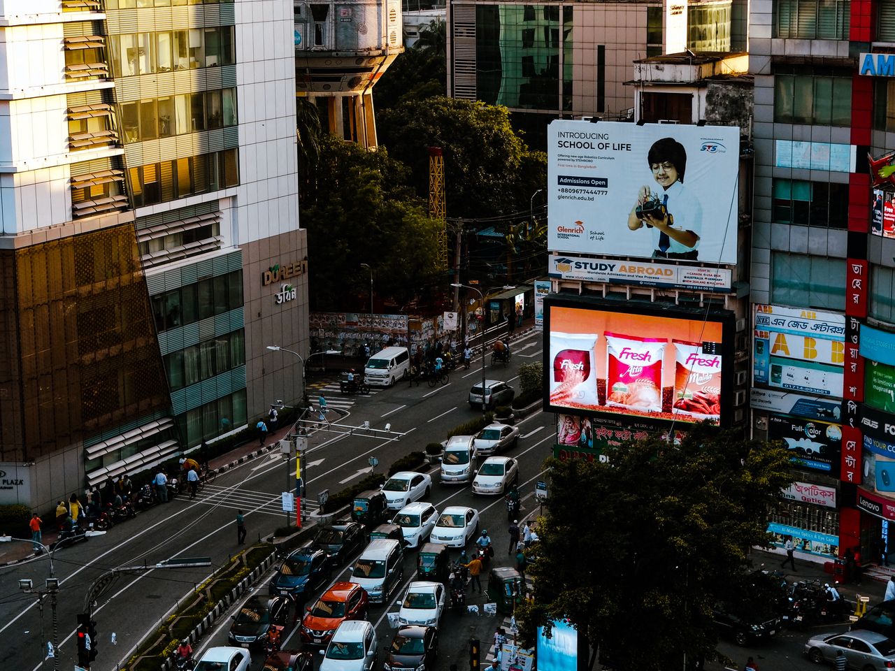 Aerial view of a bustling intersection in Dhaka, Bangladesh, showcasing urban life and vibrant advertisements.